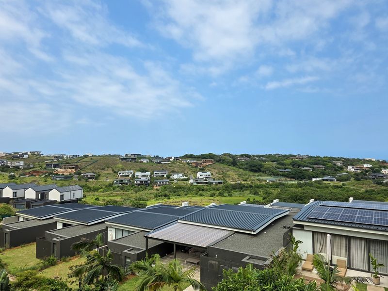Elevated view overlooking a modern residential estate with solar-equipped townhouse roofs and surrounding natural landscape.
