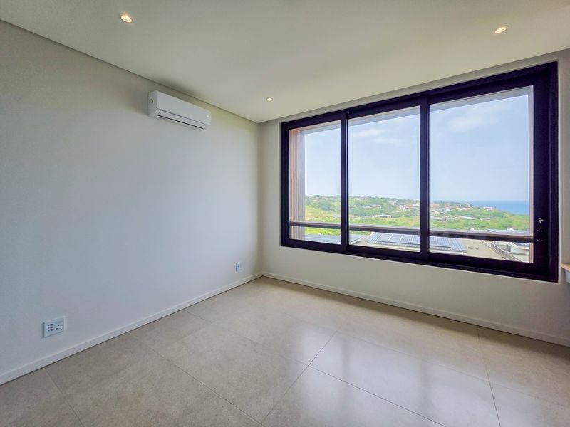A bright, modern, and empty bedroom featuring large sliding windows with scenic views, tiled flooring, and a wall-mounted air conditioning unit.