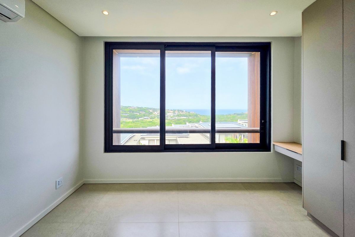 A bright, modern, and empty bedroom featuring tiled floors, built-in cupboards, a built-in desk, air conditioning, and large windows with scenic views.