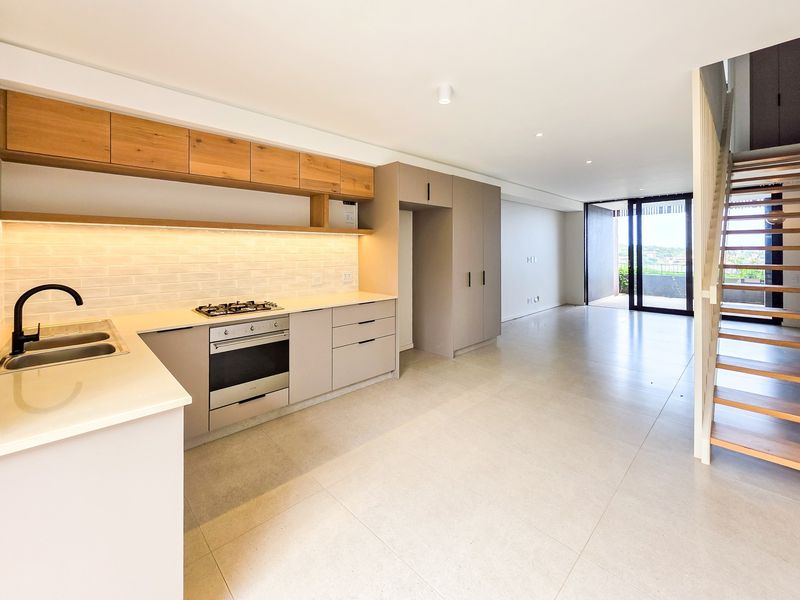Modern open-plan kitchen and living area featuring sleek cabinetry, gas hob, stone countertops, and a contemporary staircase leading to the upper level.