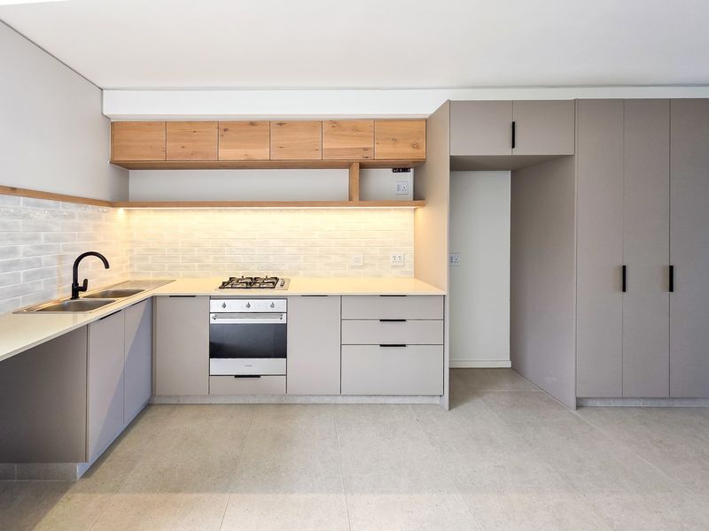 Modern kitchen featuring sleek cabinetry, stone countertops, subway tile backsplash, built-in oven, gas hob, and integrated storage in a clean, contemporary design.