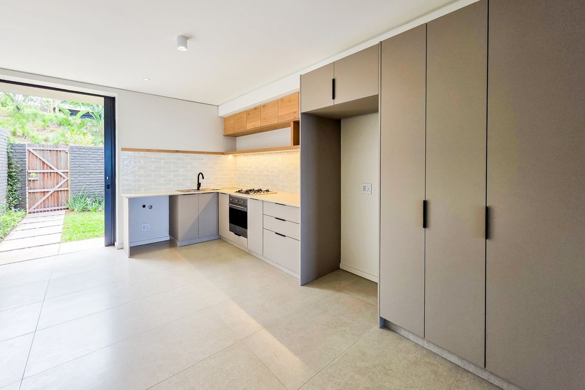 Modern kitchen featuring sleek cabinetry, subway tile backsplash, integrated appliances, and direct access to a private outdoor patio area.