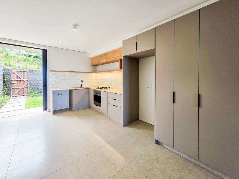 Modern kitchen featuring sleek cabinetry, subway tile backsplash, integrated appliances, and direct access to a private outdoor patio area.
