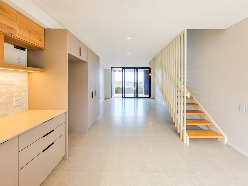 Modern open-plan living area featuring sleek cabinetry, a contemporary staircase with timber treads, and large sliding doors leading to an outdoor space.