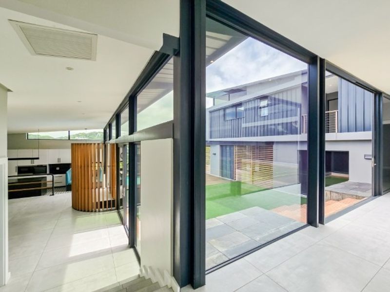 Modern open-plan living area featuring large-format floor tiles, extensive floor-to-ceiling glass walls, and seamless indoor-outdoor flow to the rear garden.