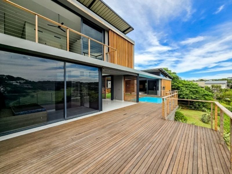 Spacious elevated timber deck featuring modern architectural design, glass balustrades, and seamless indoor-outdoor flow overlooking the swimming pool and surrounding landscape.