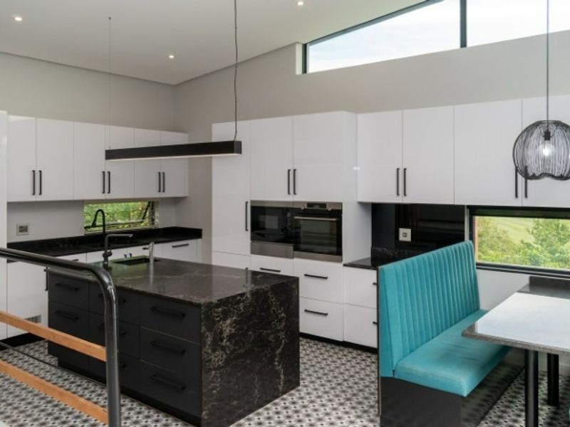Modern kitchen featuring high-gloss white cabinetry, a dark stone-topped island, built-in appliances, and clerestory windows providing natural light.