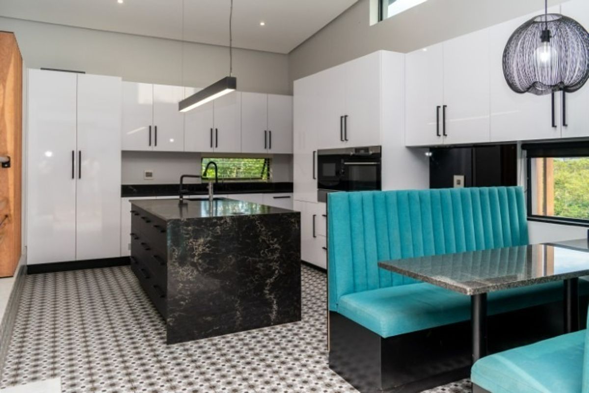 Modern kitchen featuring high-gloss white cabinetry, a dark stone island, built-in appliances, and distinctive patterned floor tiles with integrated dining seating.