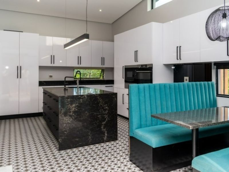 Modern kitchen featuring high-gloss white cabinetry, a dark stone island, built-in appliances, and distinctive patterned floor tiles with integrated dining seating.