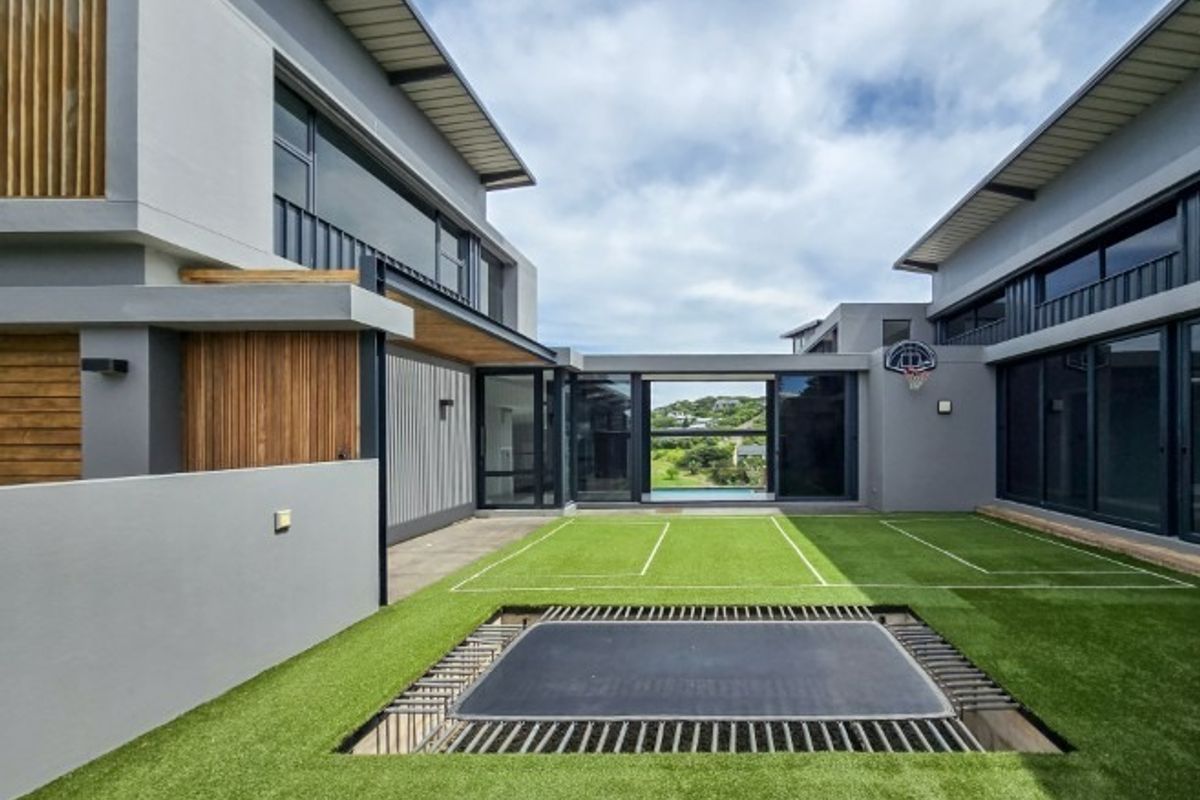 A modern rear courtyard featuring artificial turf, an integrated in-ground trampoline, and a basketball hoop, framed by contemporary architectural building wings.