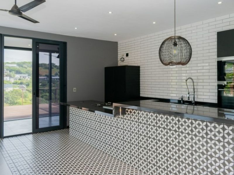 Modern kitchen featuring a patterned tile island, stainless steel countertops, subway tile backsplash, built-in oven, and direct access to an outdoor balcony.