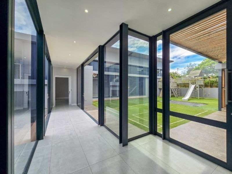 Modern, light-filled hallway featuring extensive floor-to-ceiling glass walls, tiled flooring, and direct access to the rear garden area.