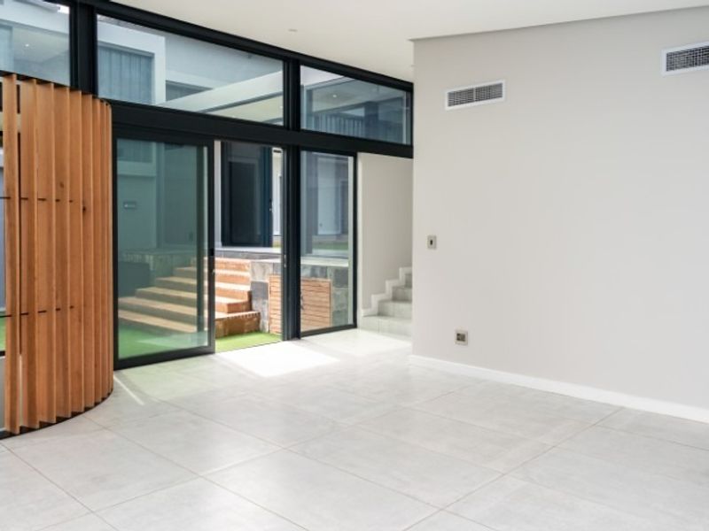 Spacious, modern living area featuring large format floor tiles, ducted air conditioning, and expansive black aluminium sliding doors opening to an outdoor courtyard.