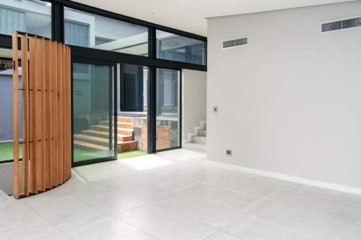 Spacious, modern living area featuring large format floor tiles, ducted air conditioning, and expansive black aluminium sliding doors opening to an outdoor courtyard.
