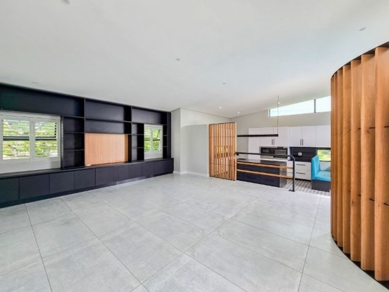 Spacious open-plan living area featuring large-format floor tiles, extensive built-in cabinetry, and a modern kitchen with a central island and timber slat divider.
