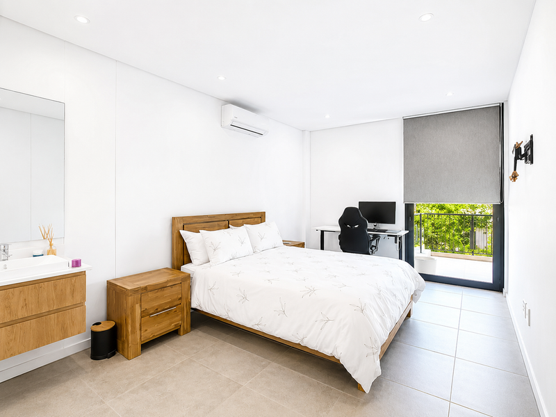 Modern bedroom featuring tiled flooring, recessed lighting, a wall-mounted air conditioning unit, and an integrated vanity with direct access to a private balcony.