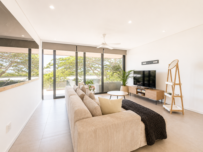 A bright and modern living room featuring large sliding glass doors, tiled flooring, recessed downlights, and a ceiling fan, offering a seamless indoor-outdoor flow.