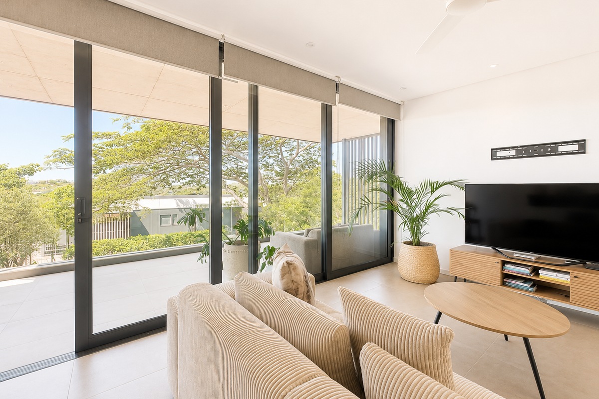 Bright living room featuring large sliding glass doors that open onto a spacious balcony, complemented by neutral tiled flooring and a modern ceiling fan.