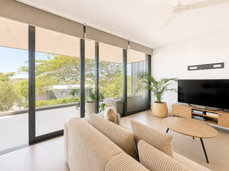 Bright living room featuring large sliding glass doors that open onto a spacious balcony, complemented by neutral tiled flooring and a modern ceiling fan.