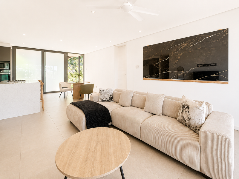 Modern open-plan living area featuring large format floor tiles, a sleek kitchen island with built-in appliances, and seamless access to the outdoor patio.