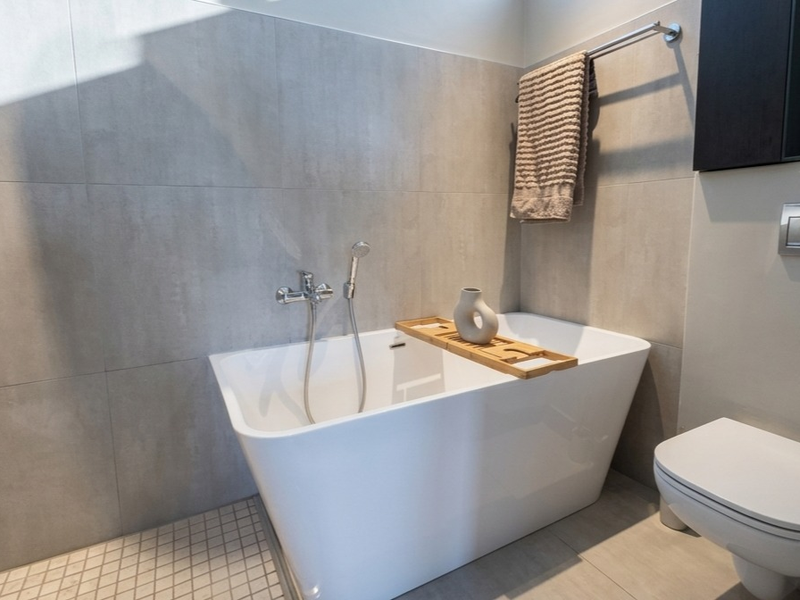 Modern bathroom featuring a sleek freestanding bathtub, wall-mounted toilet, and contemporary grey tiling throughout.