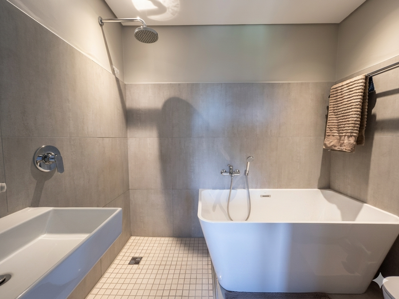 Modern bathroom featuring a sleek freestanding bathtub, wall-mounted shower fixtures, and a minimalist basin with neutral grey wall tiling.
