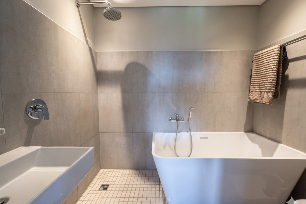 Modern bathroom featuring a sleek freestanding bathtub, wall-mounted shower fixtures, and a minimalist basin with neutral grey wall tiling.