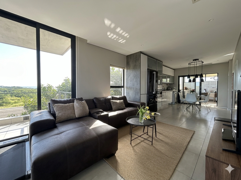 Modern open-plan living and kitchen area featuring sleek cabinetry, integrated appliances, large sliding glass doors, and abundant natural light with scenic views.