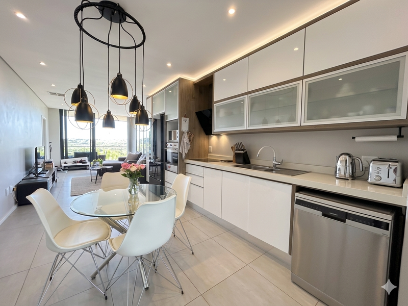 Modern open-plan kitchen and living area featuring sleek cabinetry, integrated appliances, recessed lighting, and large windows with natural light.
