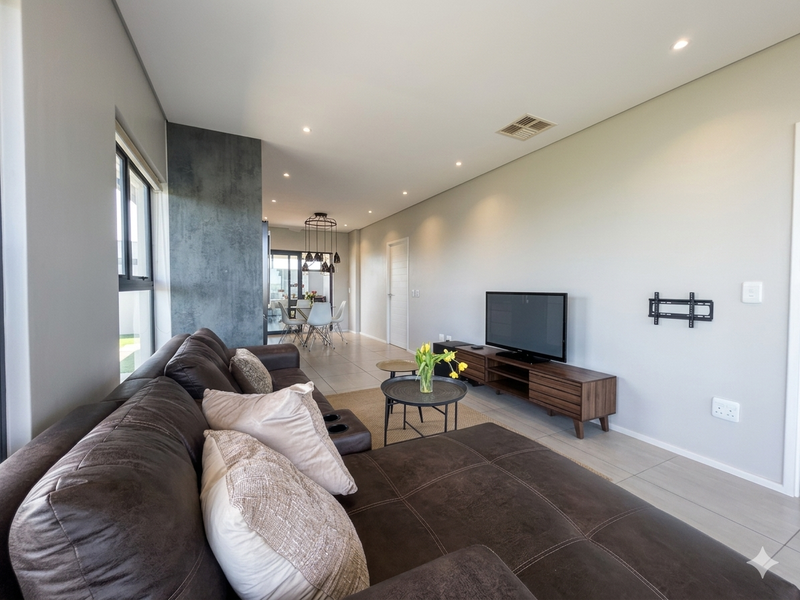 Modern open-plan living and dining area featuring neutral tiled floors, recessed lighting, and a contemporary feature wall.