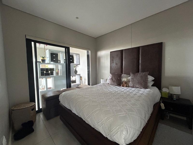 A well-maintained bedroom featuring neutral walls, tiled flooring, and a large sliding glass door providing access to an adjacent outdoor space.