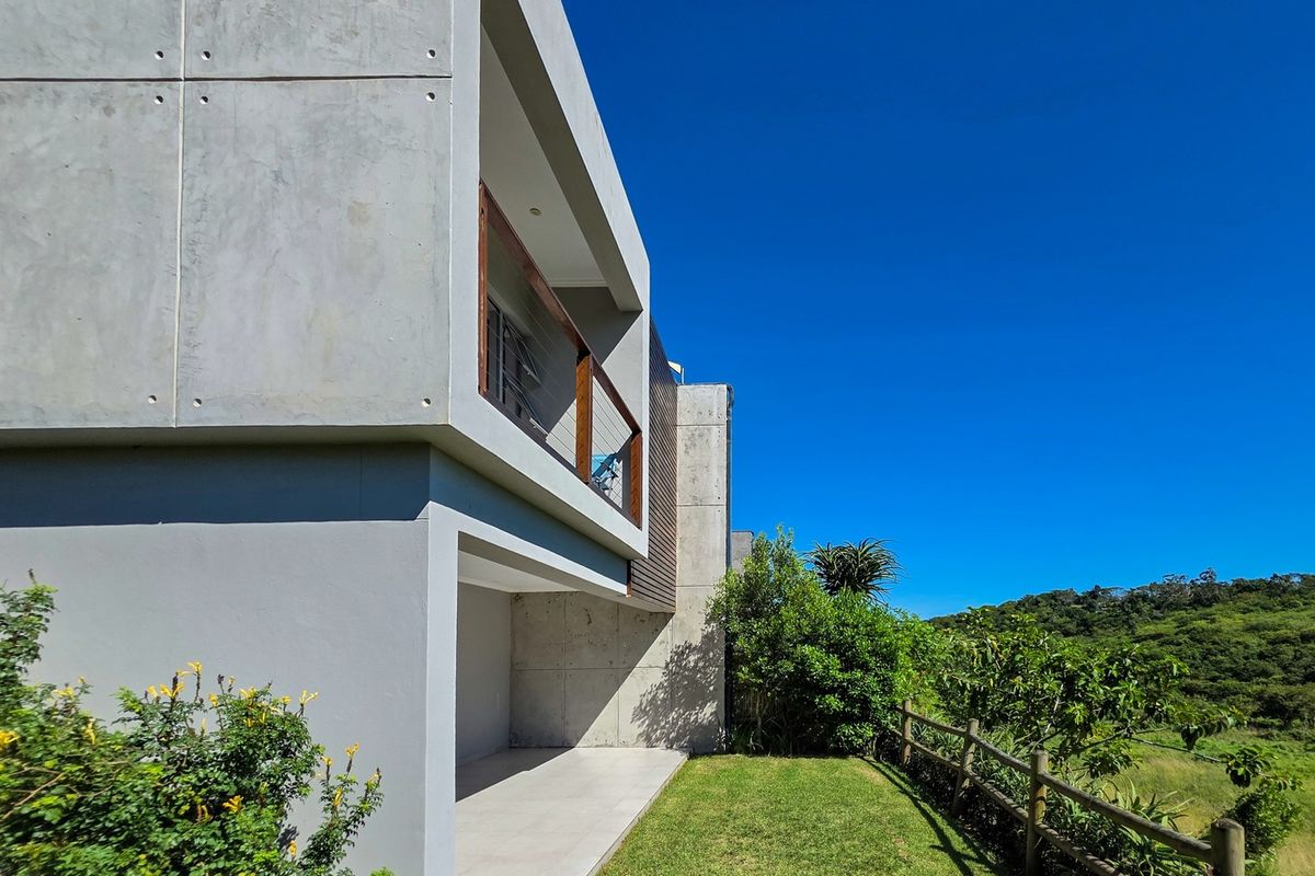 Modern townhouse rear elevation featuring a concrete facade, covered patio area, and a timber balcony overlooking a landscaped garden and natural surroundings.