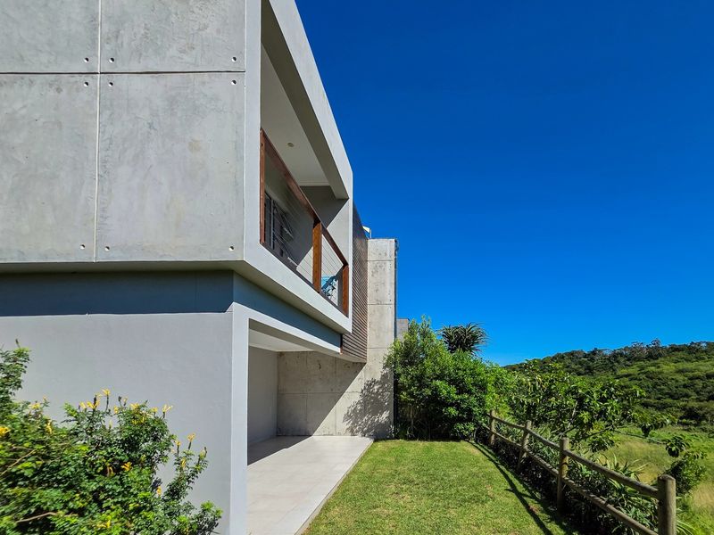Modern townhouse rear elevation featuring a concrete facade, covered patio area, and a timber balcony overlooking a landscaped garden and natural surroundings.