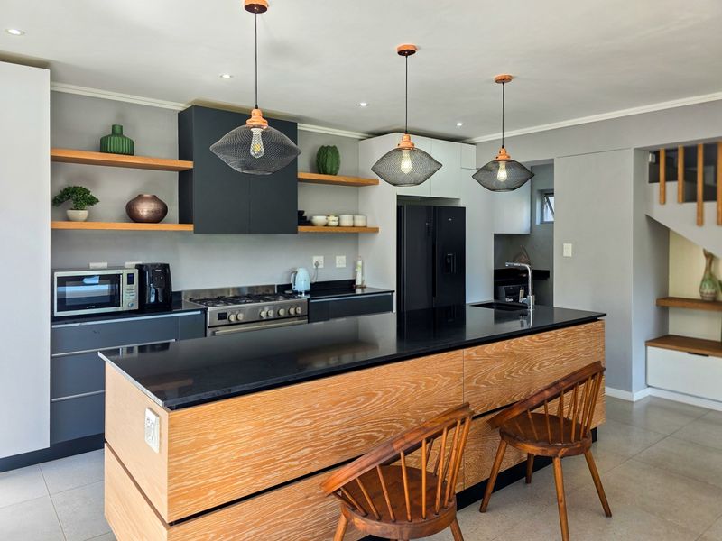 Modern kitchen featuring a large wooden island with stone countertops, gas stove, sleek cabinetry, open shelving, and stylish pendant lighting.