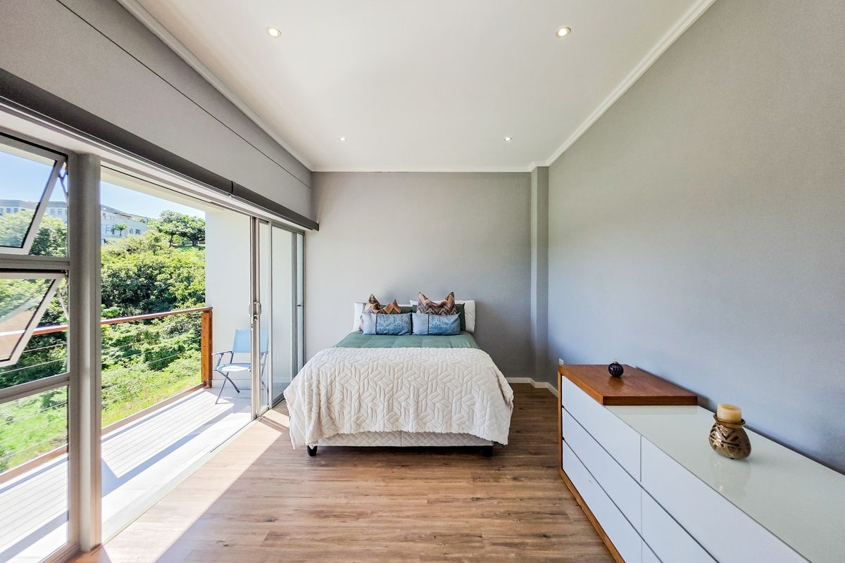 Spacious bedroom featuring modern laminate flooring, recessed lighting, and large sliding glass doors opening onto a private balcony with scenic views.