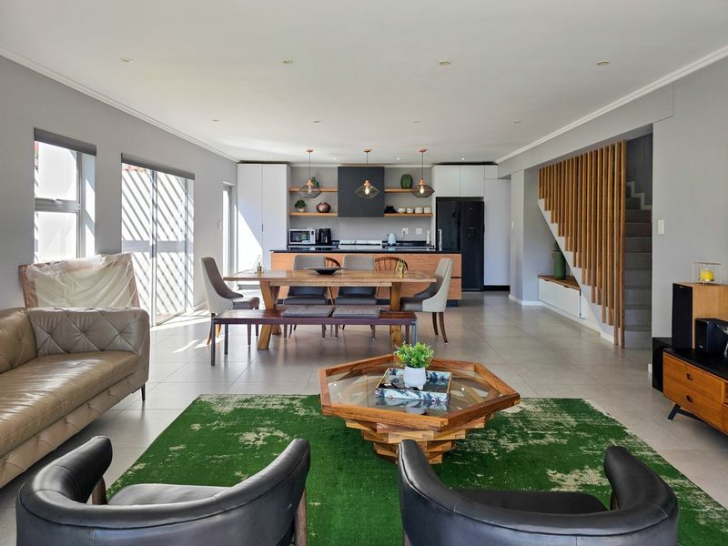 Spacious open-plan living and dining area featuring a modern kitchen with island, tiled floors, and a stylish timber slat staircase feature.
