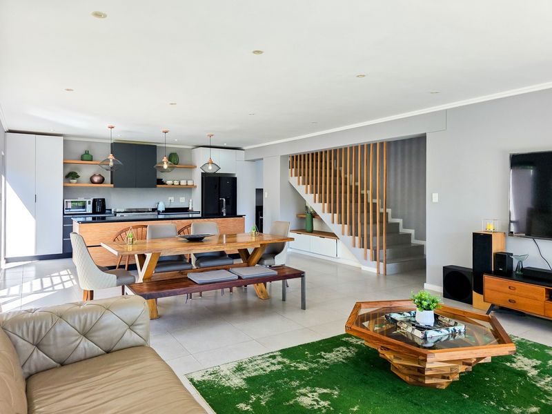 Spacious open-plan living, dining, and kitchen area featuring modern cabinetry, a central island, and a contemporary timber-slatted staircase.