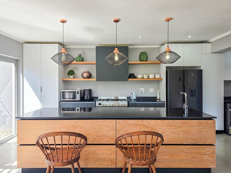 Modern kitchen featuring a large island with stone countertops, built-in gas hob, extractor fan, and sleek cabinetry with floating shelving.