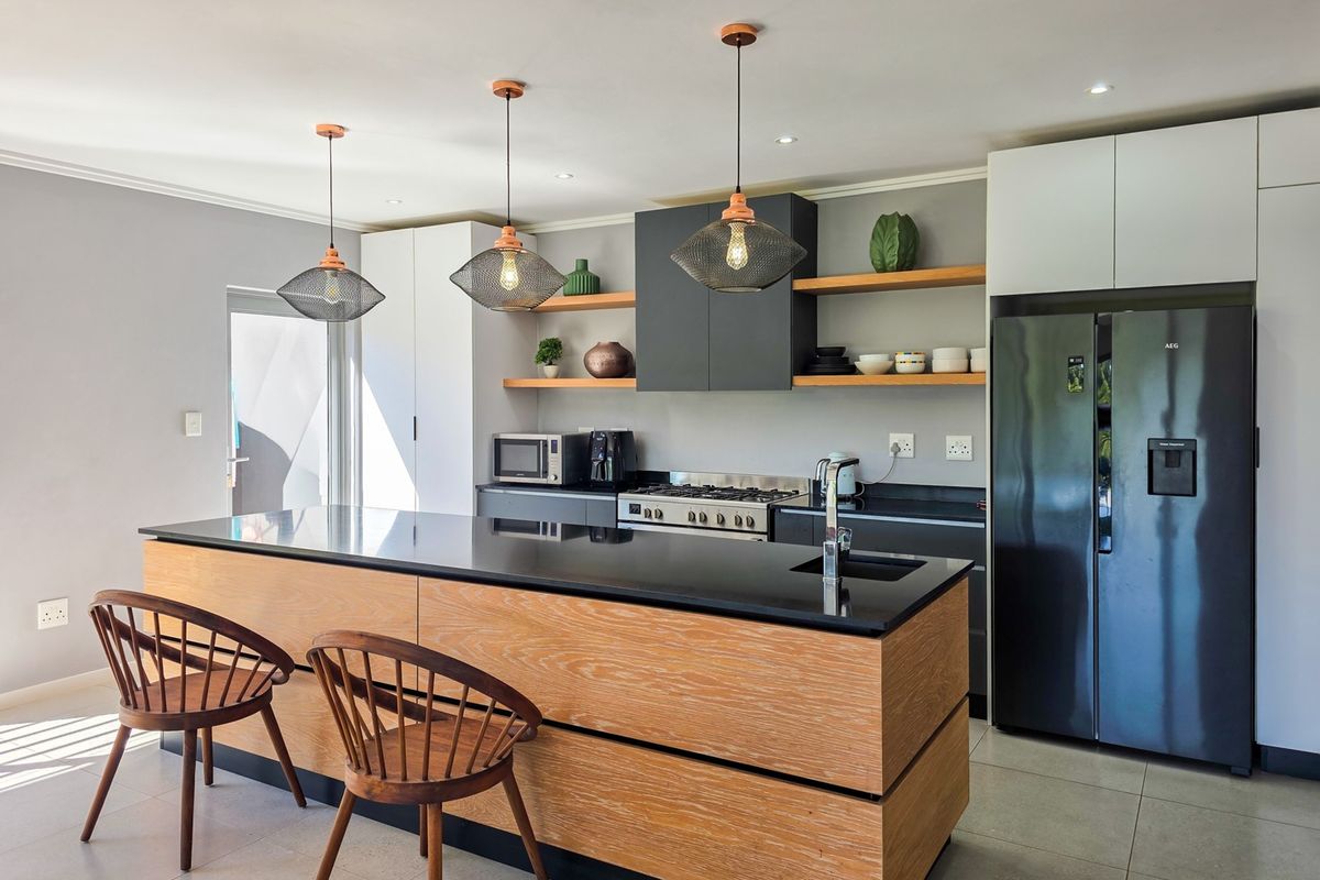Modern kitchen featuring a large wooden island with stone countertop, gas stove, integrated cabinetry, and stylish pendant lighting.