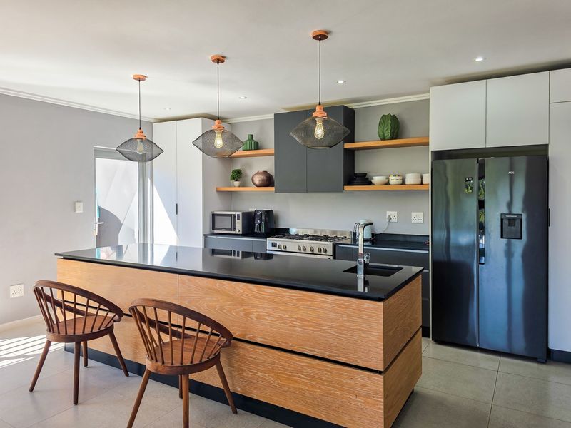 Modern kitchen featuring a large wooden island with stone countertop, gas stove, integrated cabinetry, and stylish pendant lighting.