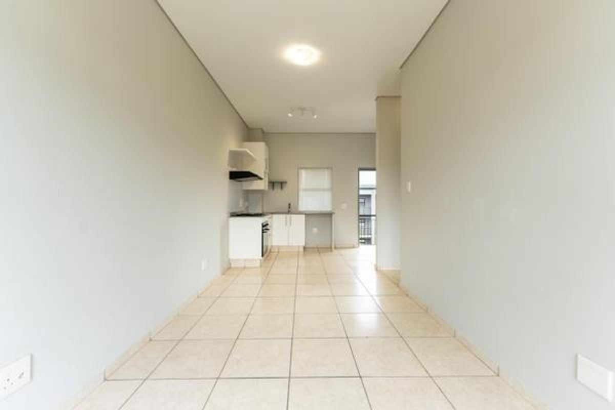 An open-plan living and kitchen area featuring neutral tiled flooring, built-in cabinetry, and integrated kitchen appliances in a clean, vacant space.