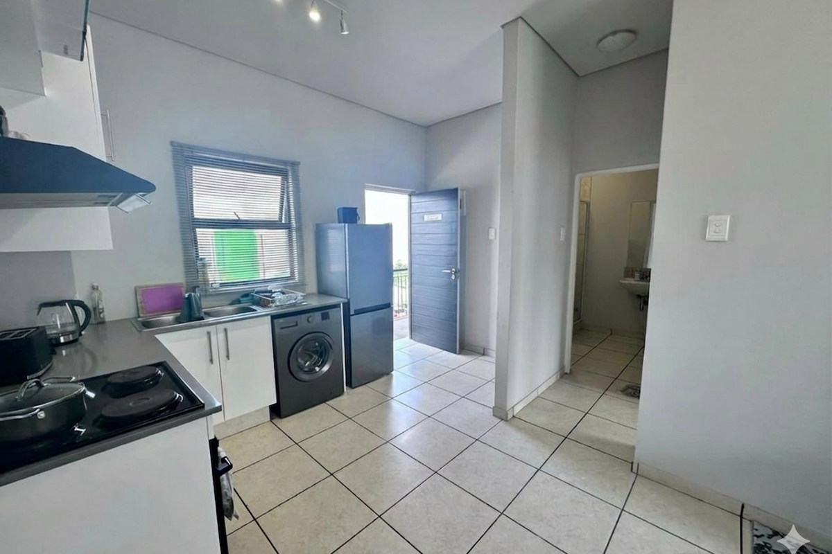 Functional kitchen featuring white cabinetry, stainless steel sink, electric hob with extractor fan, and tiled flooring, with direct access to an exterior door.
