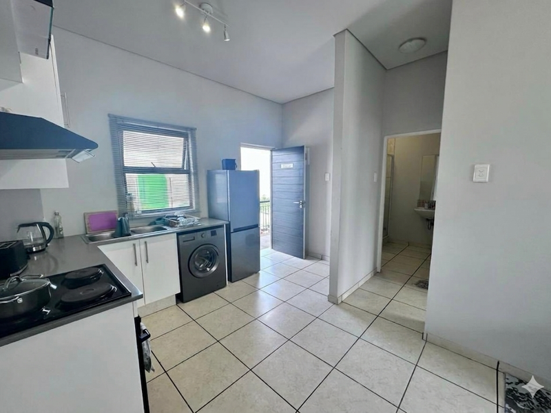 Functional kitchen featuring white cabinetry, stainless steel sink, electric hob with extractor fan, and tiled flooring, with direct access to an exterior door.