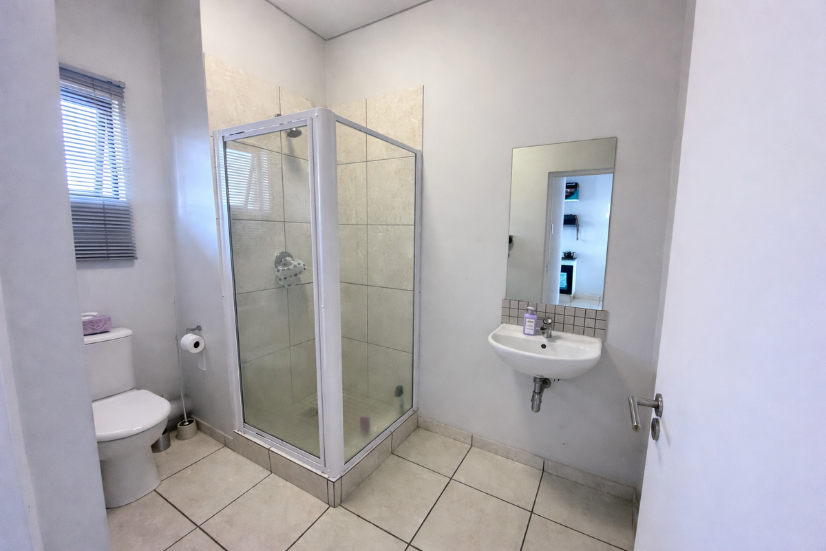 A clean and functional bathroom featuring a corner shower enclosure, wall-mounted basin, and tiled flooring.