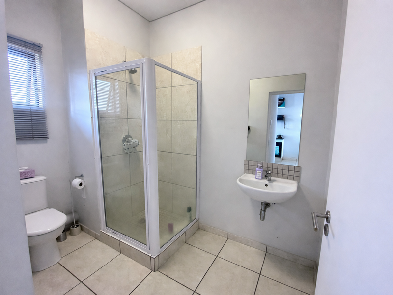 A clean and functional bathroom featuring a corner shower enclosure, wall-mounted basin, and tiled flooring.