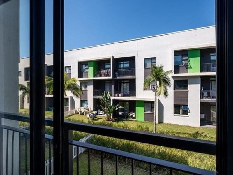 A view from a balcony overlooking a well-maintained apartment complex with landscaped gardens and modern building architecture.