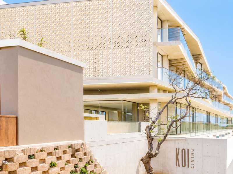 Modern architectural apartment building exterior featuring a decorative breeze block screen, glass balconies, and clean concrete finishes overlooking a water feature.