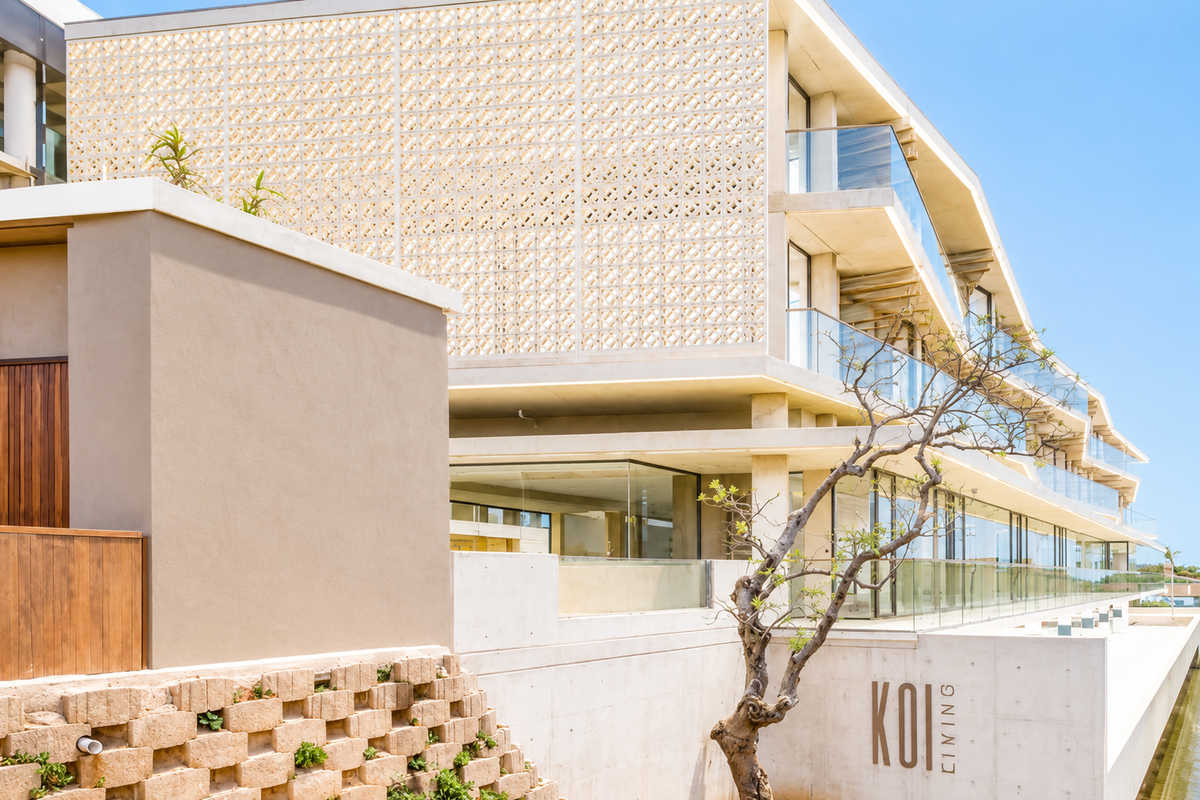 Modern architectural apartment building exterior featuring a decorative breeze block screen, glass balconies, and clean concrete finishes overlooking a water feature.