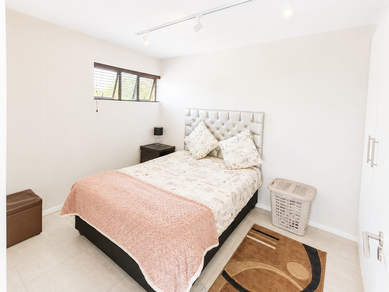 A bright bedroom featuring tiled flooring, track lighting, horizontal window blinds, and a built-in wardrobe.