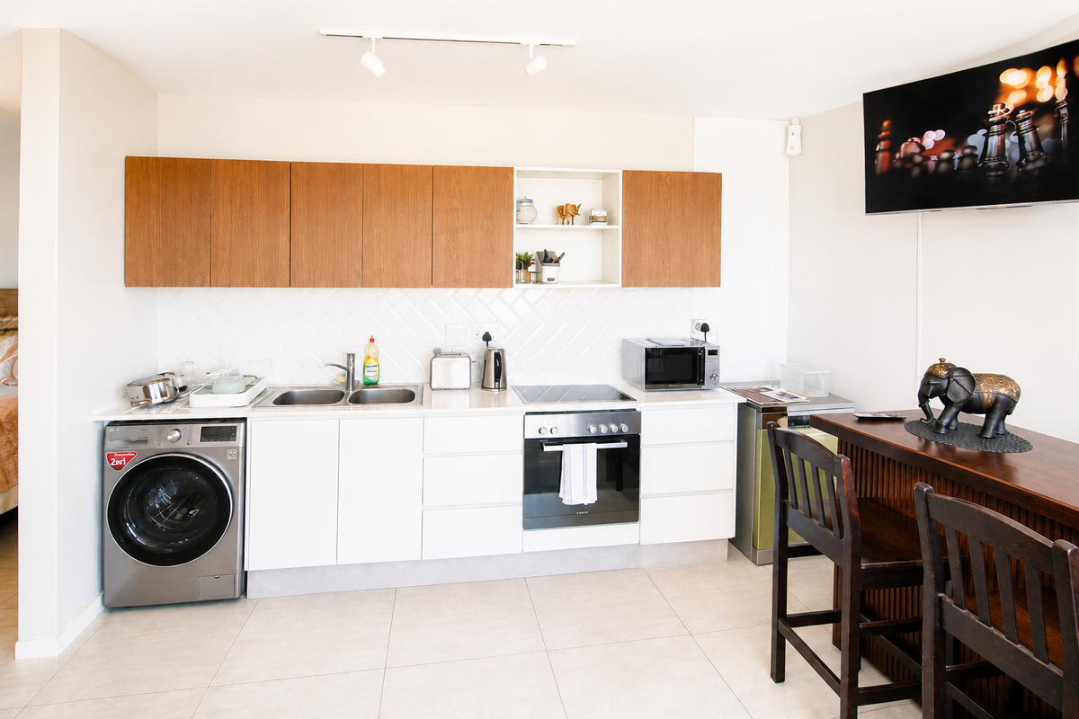 Modern kitchen featuring sleek white cabinetry, wood-tone upper cabinets, integrated oven and hob, and tiled flooring with a clean, functional layout.